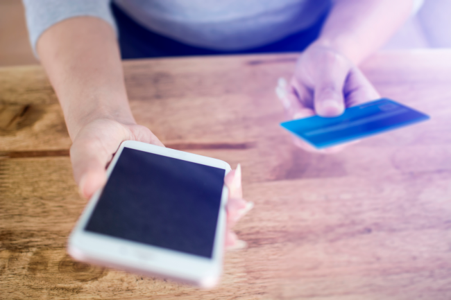 携帯電話を使用しているときにクレジットカードを手に持っている人。