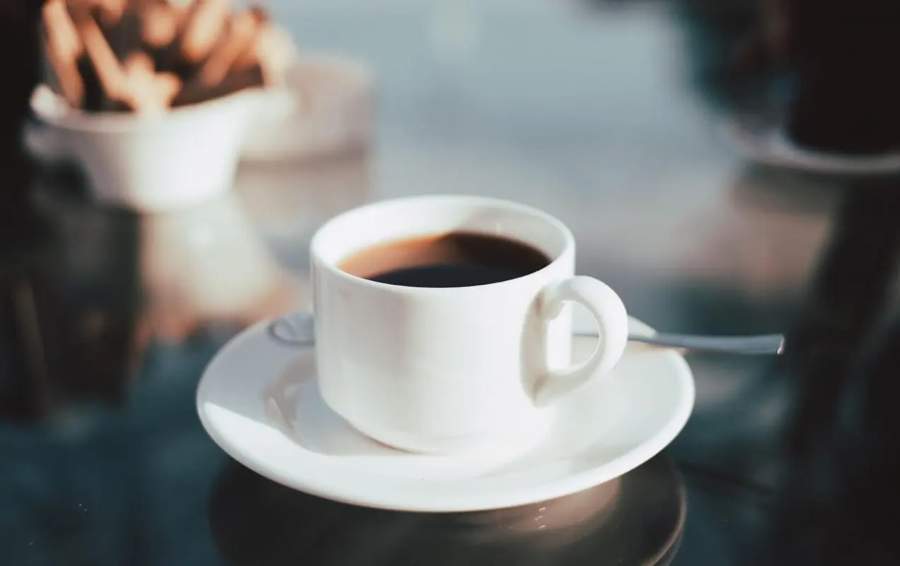โต๊ะกระจกสะท้อนแสงพร้อมถ้วยกาแฟสีขาวสั้น ๆ ที่เต็มไปด้วยกาแฟดำนั่งบนจานรองสีขาว