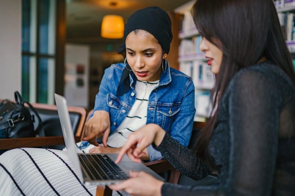 dua wanita melihat dan menunjuk laptop macbook