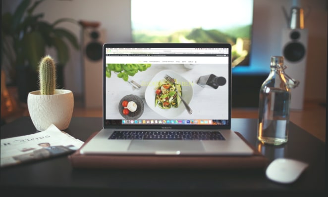laptop com um site de restaurante puxado na tela em uma mesa entre um cacto e uma garrafa de vidro com água