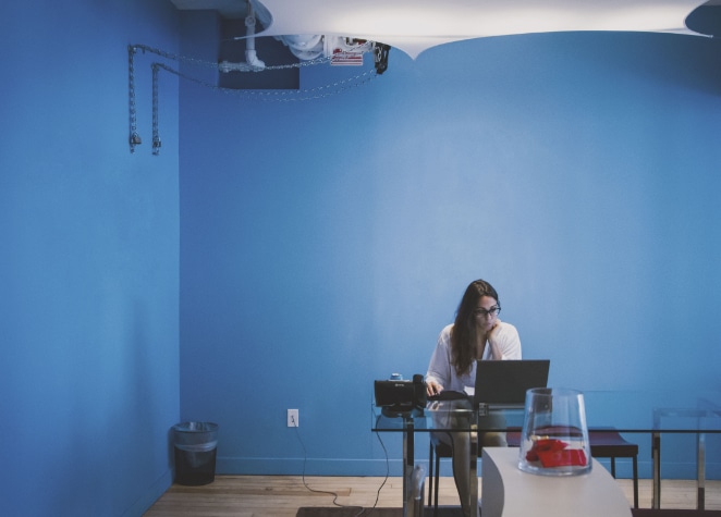 mulher trabalha em um computador em uma mesa de vidro em uma sala azul