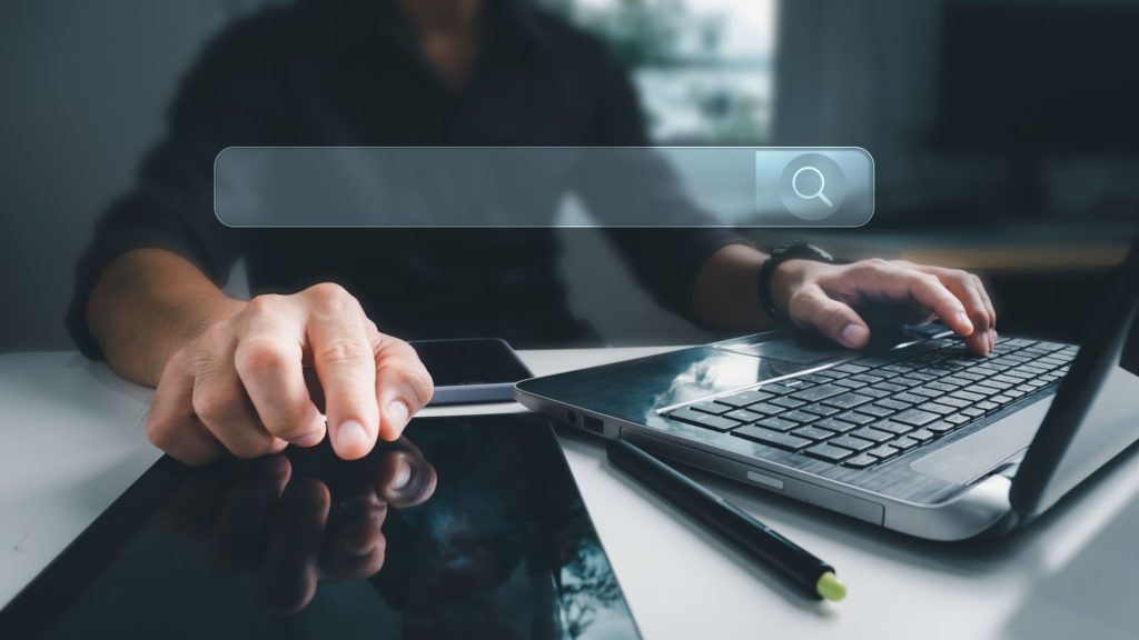 um homem navega em lojas online em um laptop. Uma sobreposição de uma barra de pesquisa vazia está na vanguarda da imagem