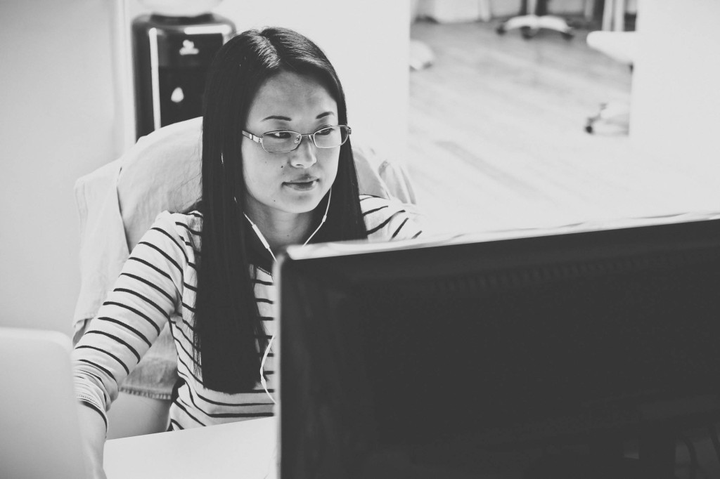イヤフォンを装着してコンピューターで作業している女性の白黒写真