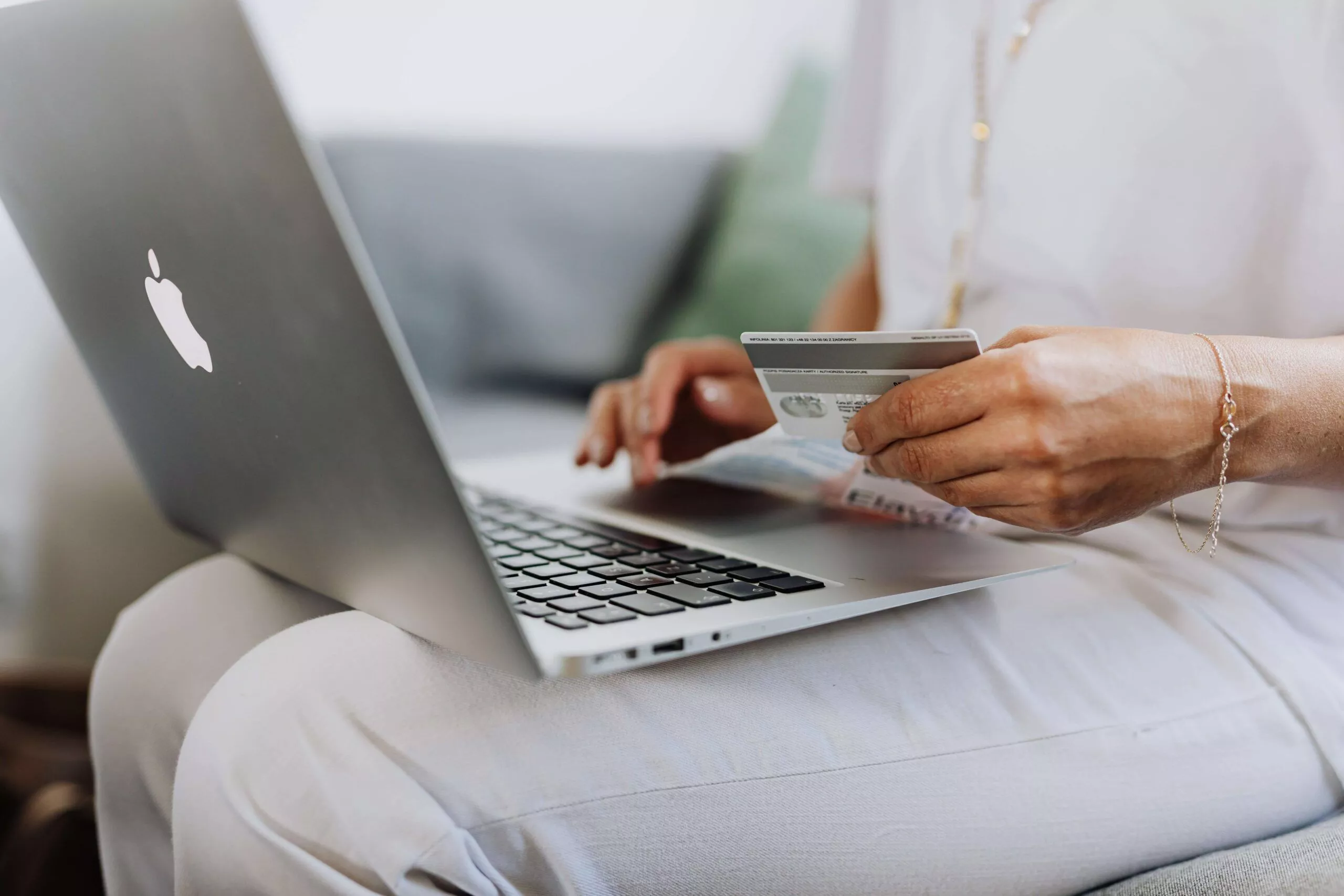 Uma pessoa usando um Macbook e segurando um cartão de crédito